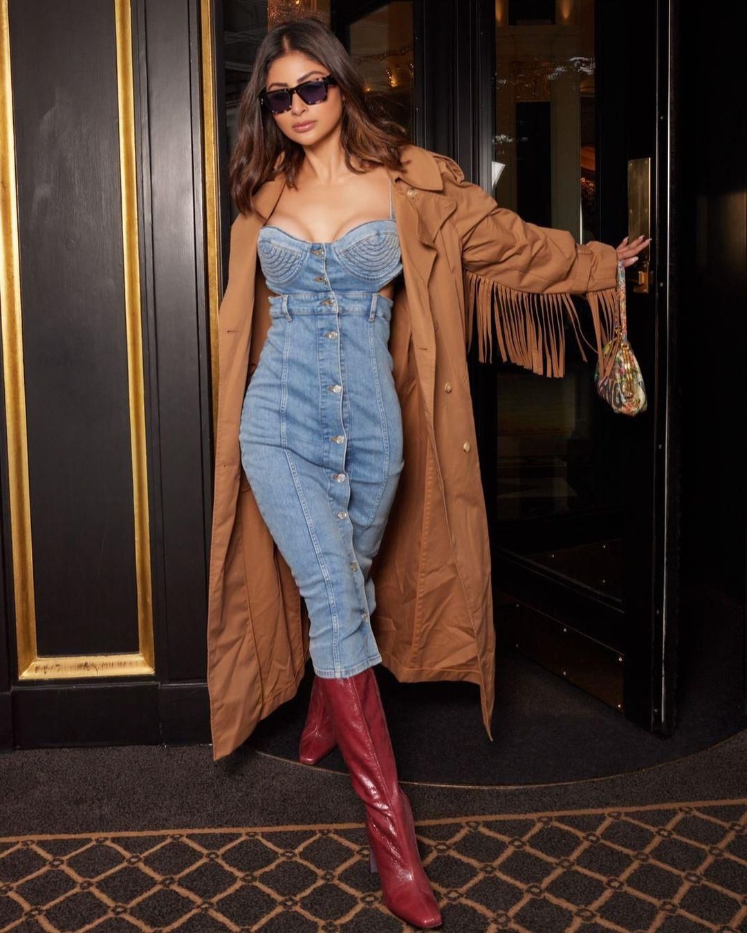 Mouni can be seen wearing a chic denim dress paired with a stylish trench coat and red boots.