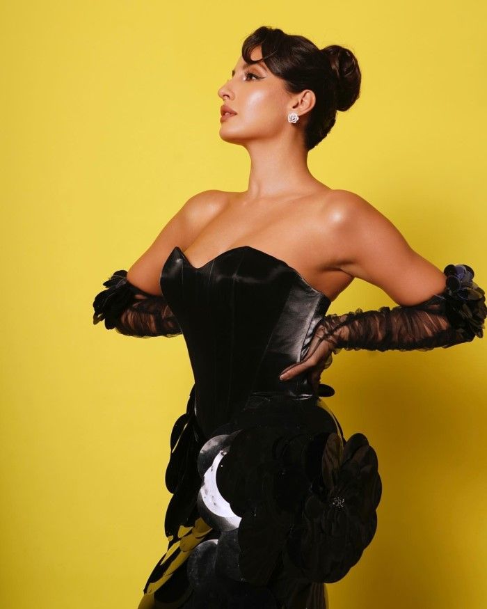 Bold Hair and Makeup: Nora complements the outfit with a neatly styled updo and bold makeup, featuring well-defined eyeliner and a nude lip.
