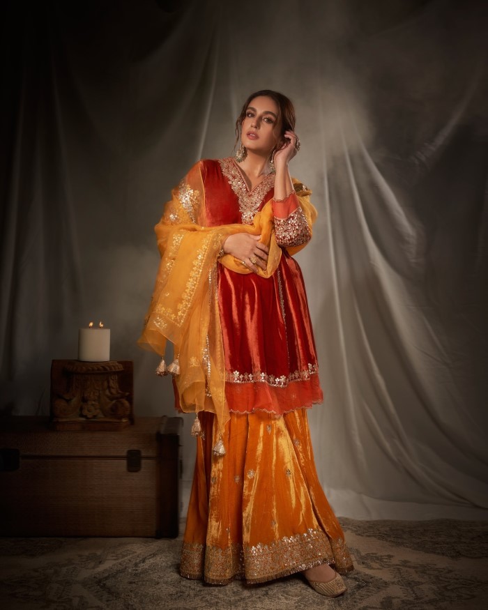 Huma Qureshi dazzles in a deep red velvet kurta adorned with intricate gold embroidery on the neckline, sleeves, and hem, exuding a sense of regal elegance and sophistication.
