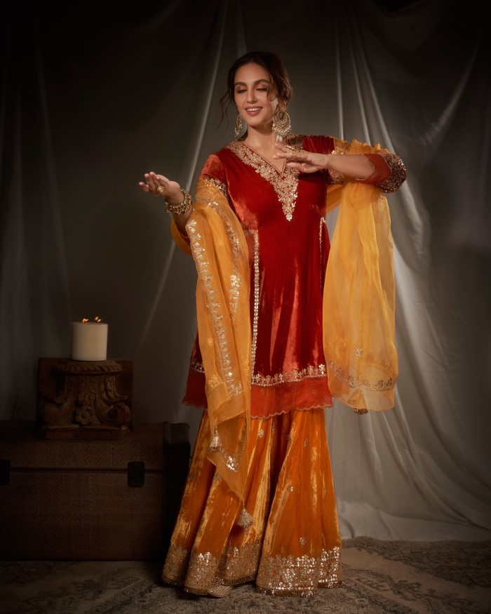 The rich red kurta is beautifully complemented by a mustard yellow lehenga, also featuring delicate gold embroidery along the hem, adding a vibrant contrast to the ensemble.