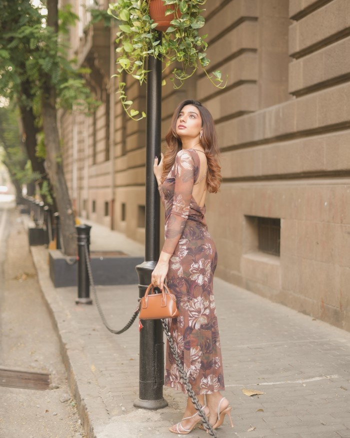 The dress highlights an open back design with elegant thin straps crossing over, adding a touch of sophistication and allure.
