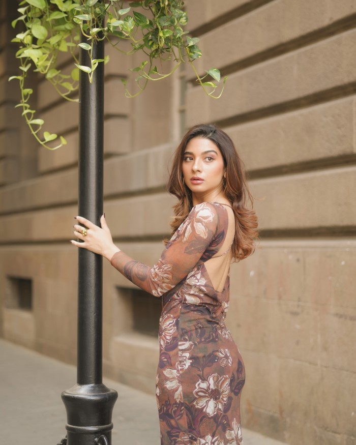 Natasha poses next to a black lamppost, with a stone wall and greenery in the background, creating a picturesque and charming scene.