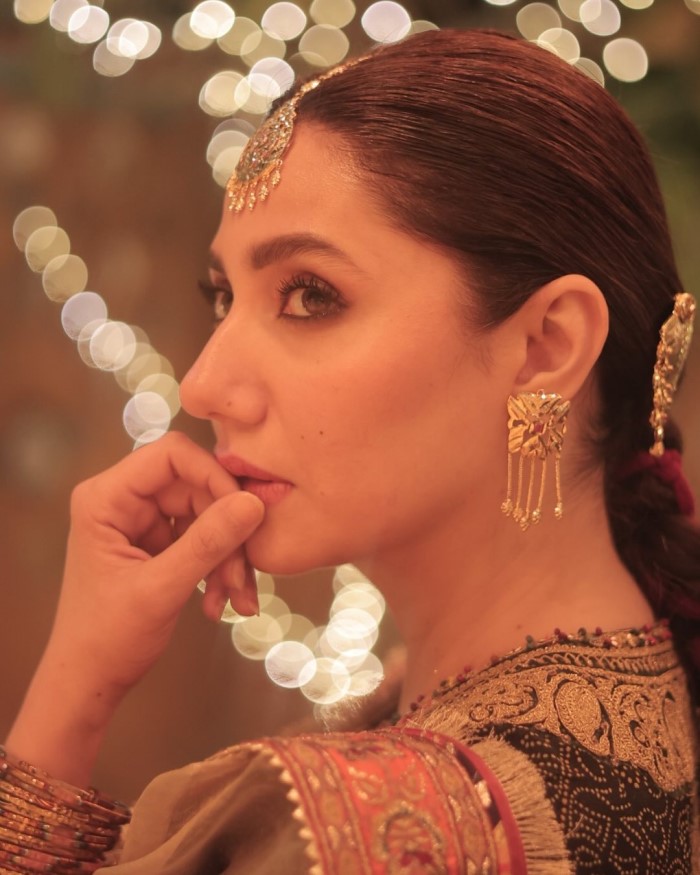 Her hair is styled in a neat braid adorned with a pink parandii, and her makeup is soft and dewy, highlighting her natural beauty and completing the look.