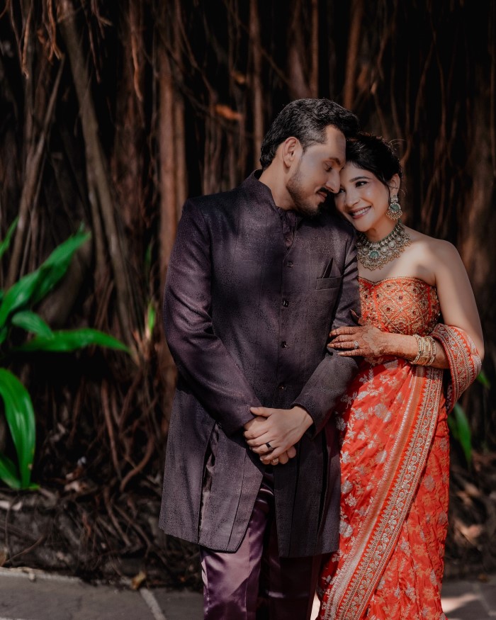 The shoot is set against a lush green backdrop, complementing the couple's attire and adding a natural charm to the photos.