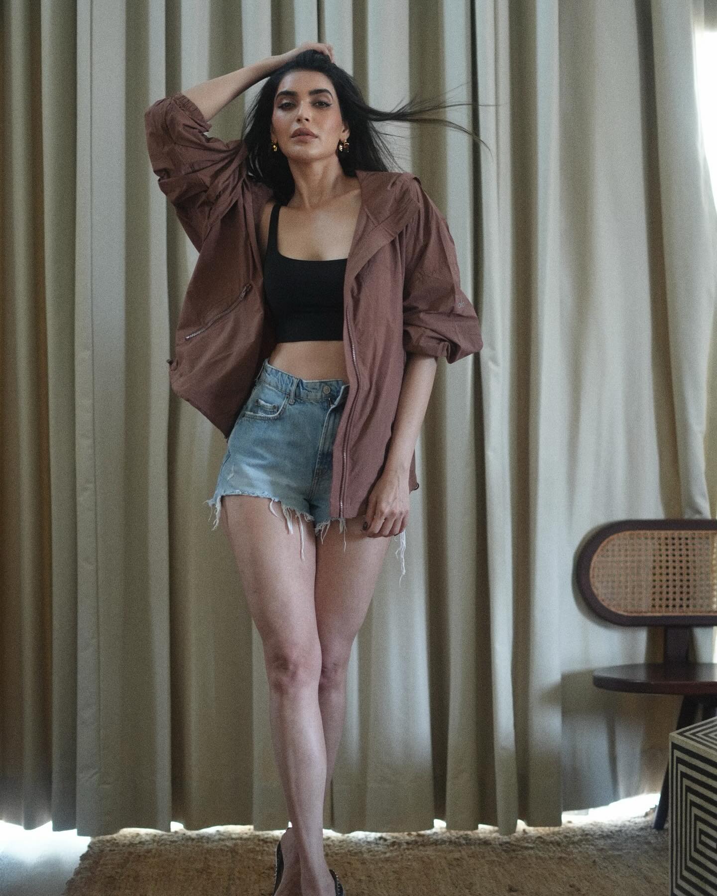 Karishma Tanna sports a relaxed yet stylish look, pairing a black crop top with high-waisted, distressed denim shorts.