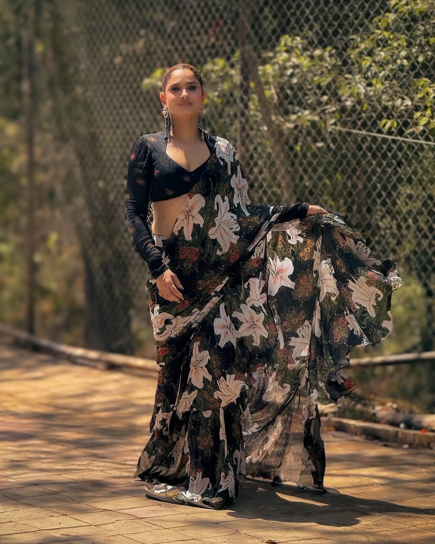 Ankita stuns in a sheer black saree adorned with large white lily prints and hints of earthy red and green tones