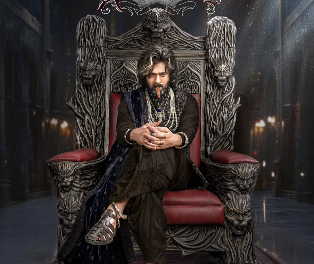 In The RajaSaab, Prabhas embraces a stylish yet mysterious look. He sports long, wavy hair, a sharp beard, and trendy outfits, exuding a royal yet contemporary charm.