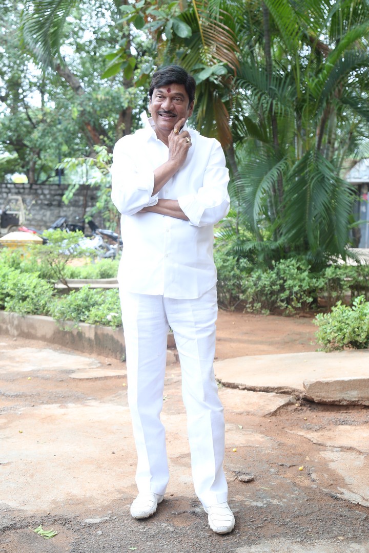 Rajendra Prasad's joyful demeanor and elegant white attire radiate timeless charm in a lush, green setting