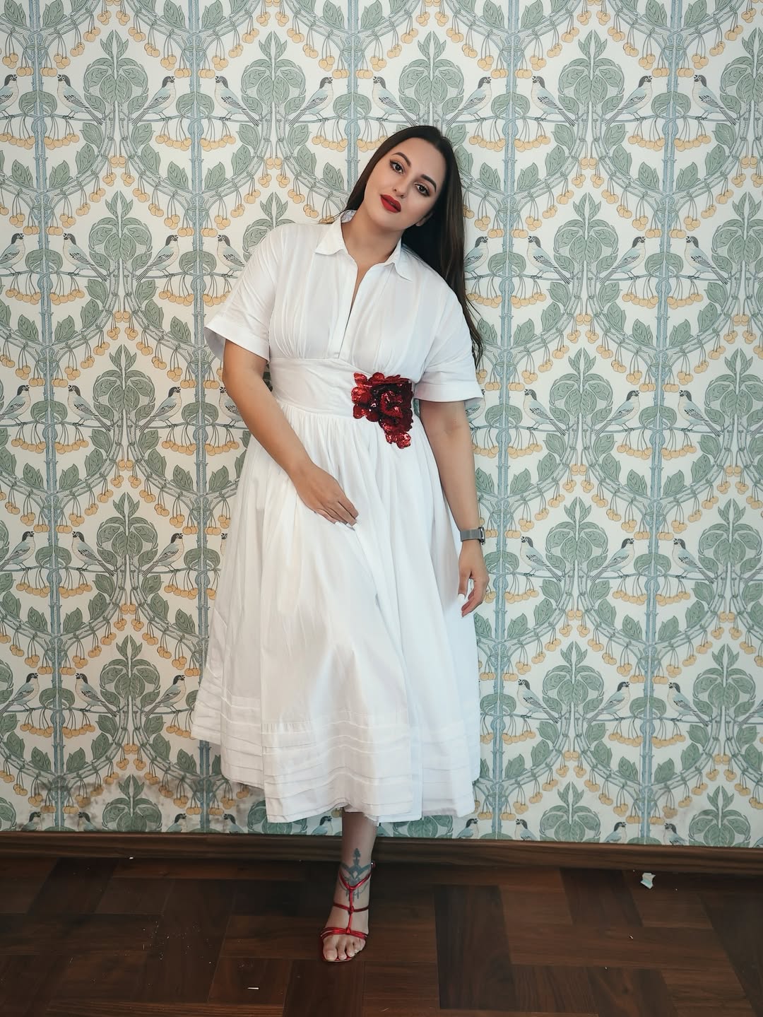 Sonakshi Sinha exudes timeless elegance in a crisp white dress with a bold red floral accent–proof that style and humor are always in fashion, even when the face is blurred!