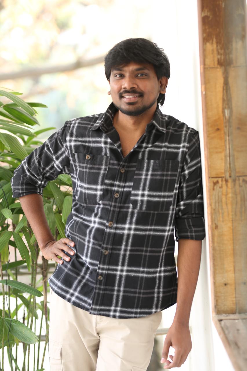 Sudheer Sriram smiling in stylish plaid outfit