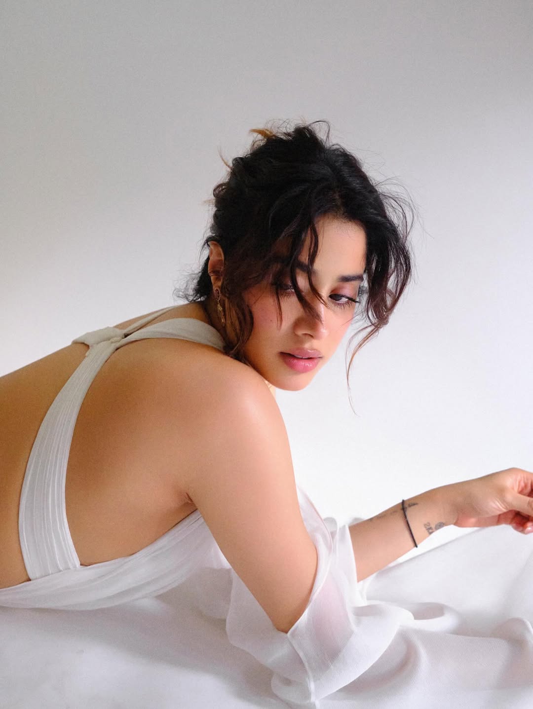 Janhvi Kapoor posing in a white backless dress with crisscross straps and soft waves hairstyle.