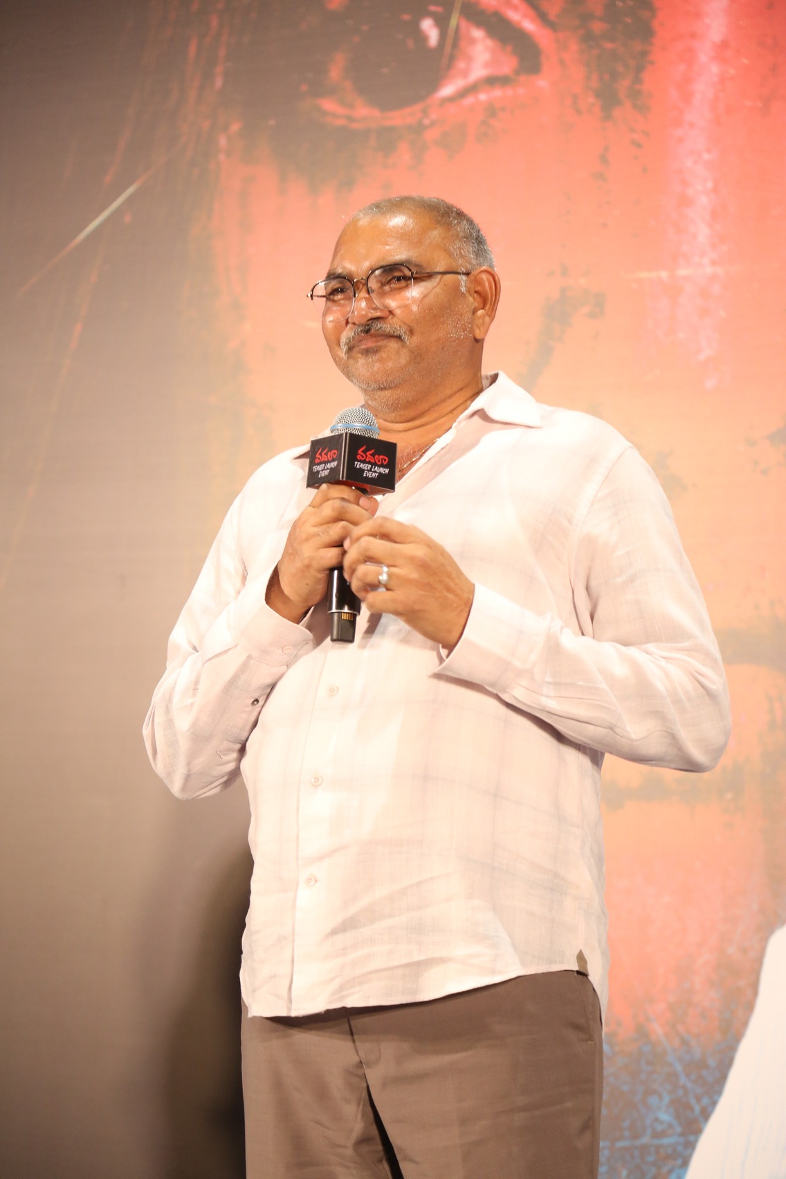 Producer Kishore Naidu speaking on stage at Vadhala teaser launch event