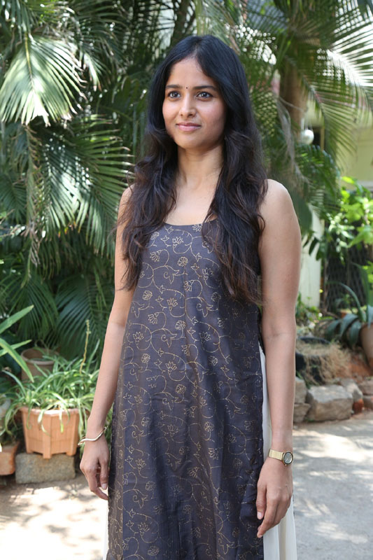 Shalini Kondepudi posing in a floral-patterned dress amidst a lush green outdoor setting.